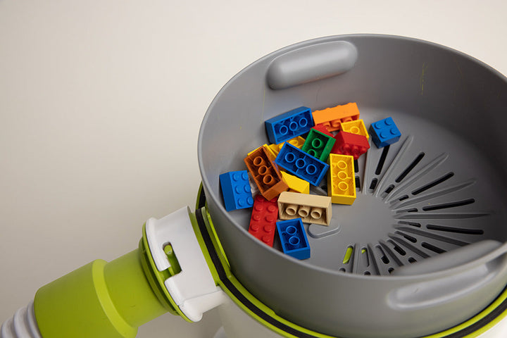 The Pick-Up Bricks lego vacuum is a portable easy-to-use device that sucks up lego and other small toys. With the clear domed top removed, you can see how the picked-up legos sit in the slotted gray collection basket that allows dust and dirt to be pulled away into a 2nd filter below.